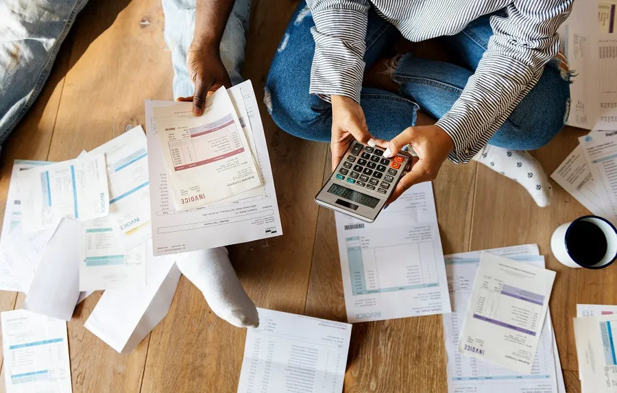 Two people sat on the floor, surrounded by bills