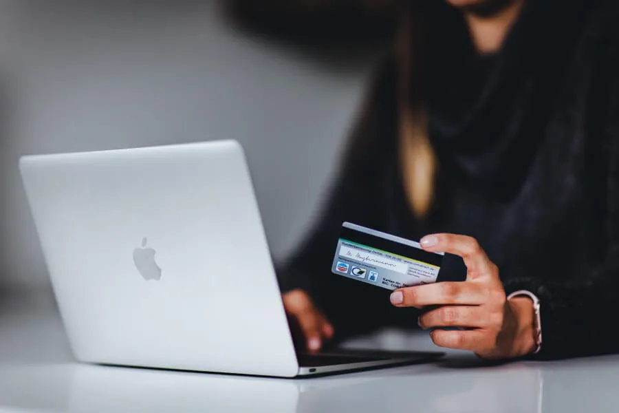 Woman shopping online, holding a credit card at a laptop