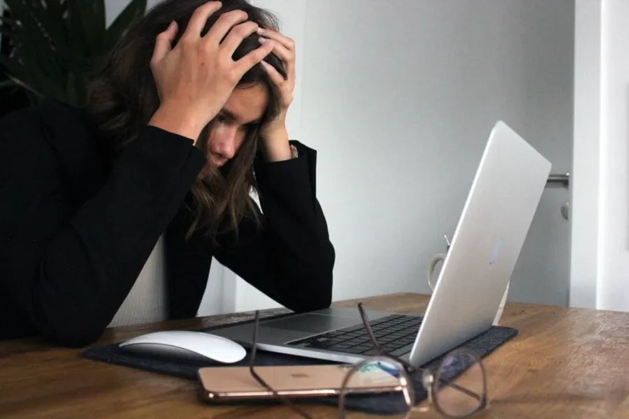Problem debt - brunette woman holding her head in worry, looking at a laptop