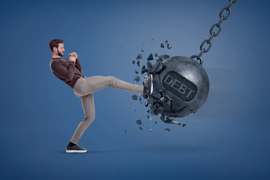 Man kicking a wrecking ball with debt on it