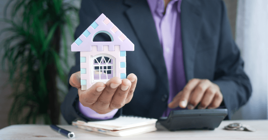 man in a suit holding a small plastic house