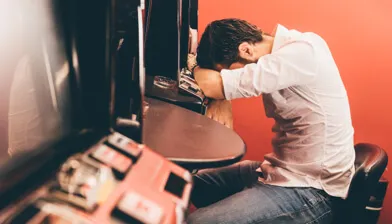 Sad man resting his head on a gambling fruit machine