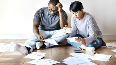 A concerned couple, sat on the floor looking at bills