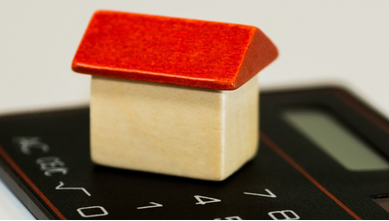 Small wooden toy house sat on top of a calculator