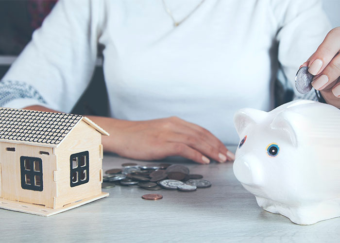 woman putting coins into her piggy bank next to a small model of a house