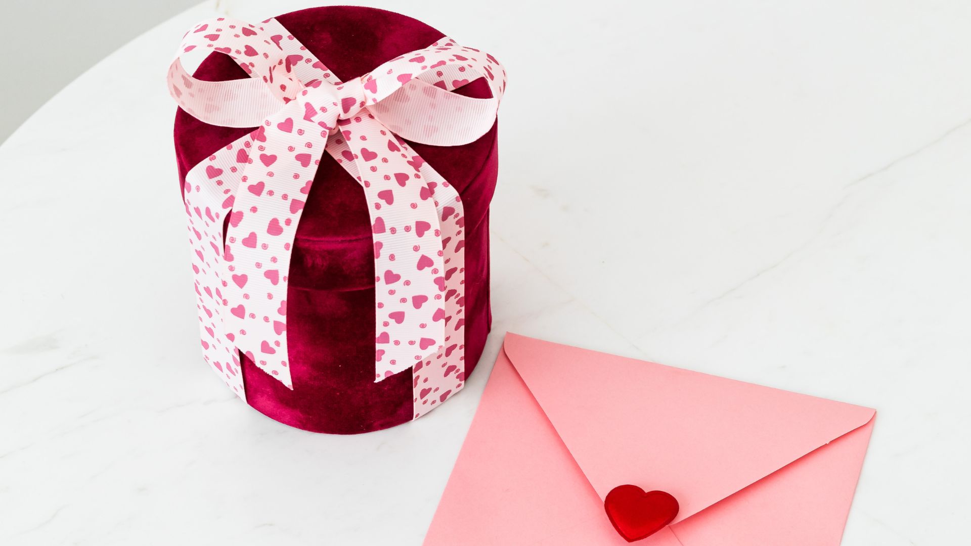 image of a valentine's day gift wrapped in heart print ribbon and a pink envelope sealed with a heart